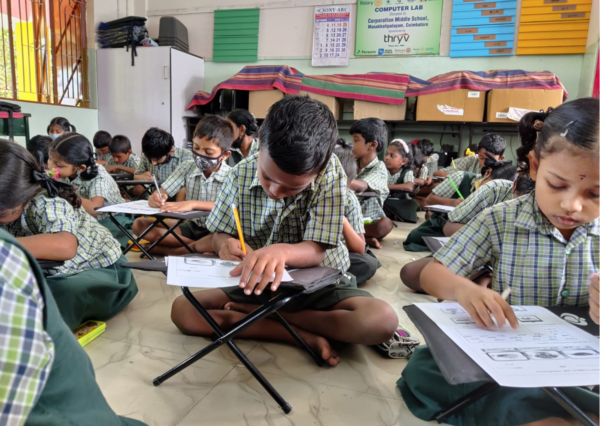 children in government school sitting on floor and writing